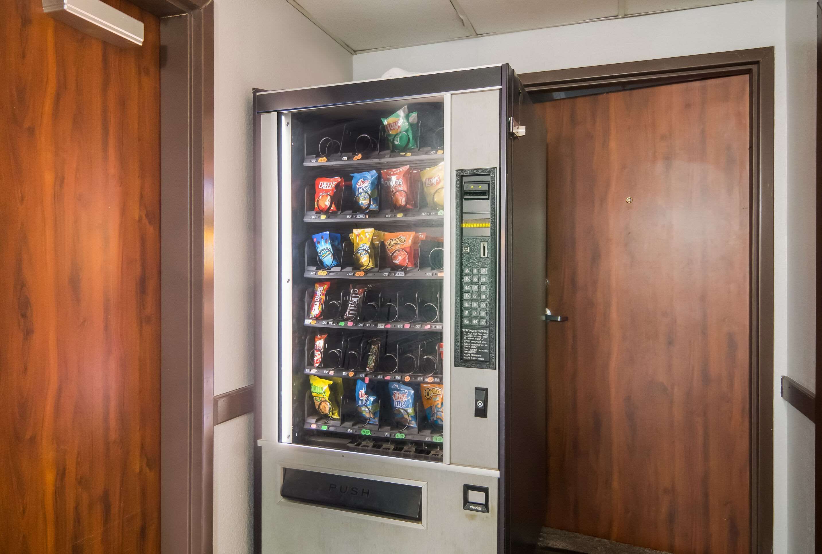 A vending machine with snacks and drinks in a room with wooden walls and a door.