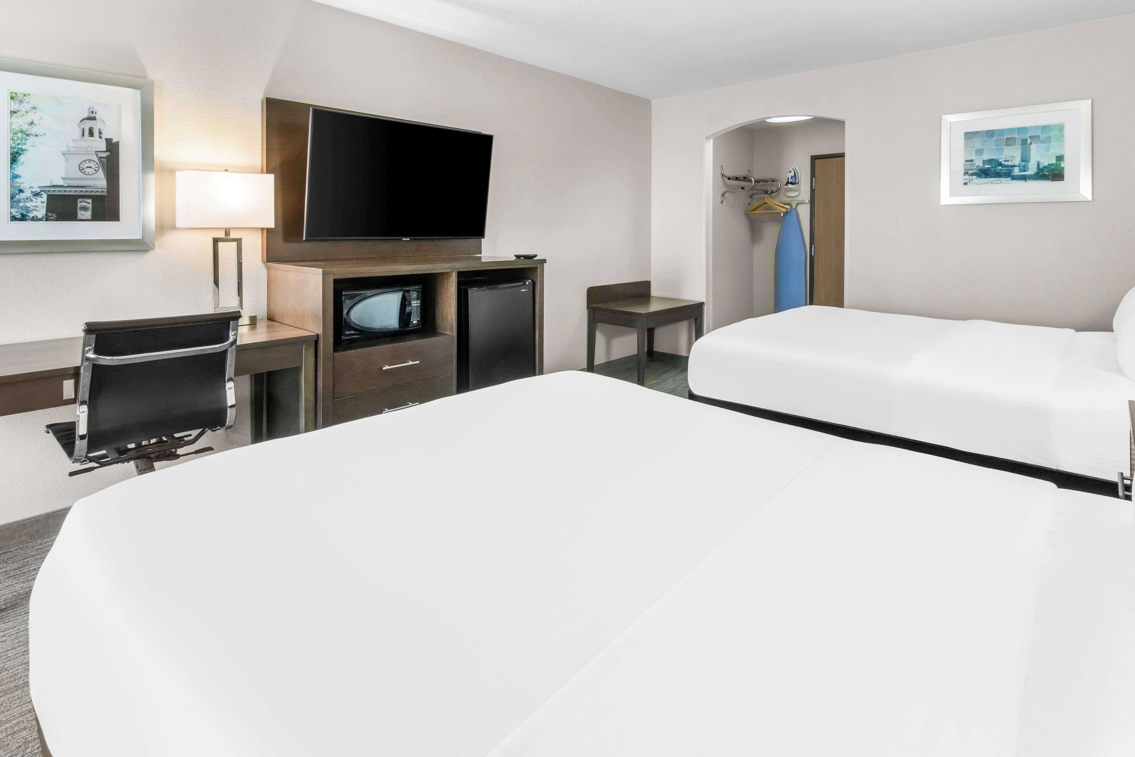Habitación de hotel con una cama grande, un escritorio con silla, un televisor y un refrigerador pequeño.