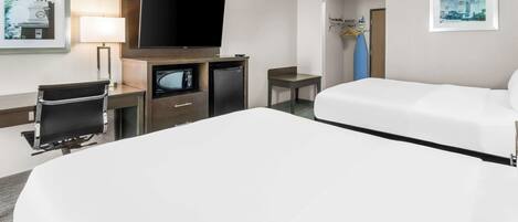 Habitación de hotel con una cama grande, un escritorio con silla, un televisor y un refrigerador pequeño.