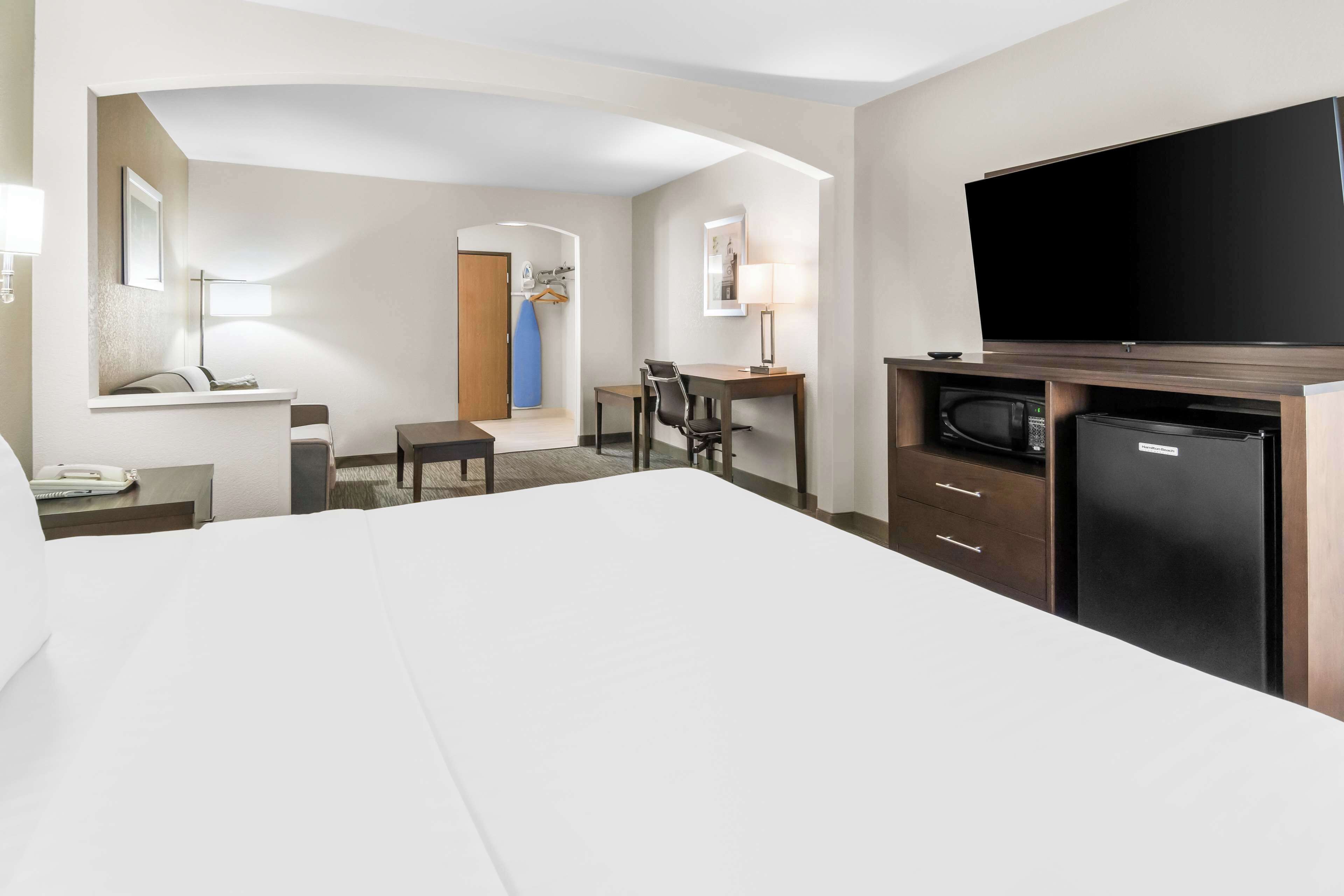A hotel room with a large bed, a desk with a chair, a television, a microwave, and a small refrigerator.