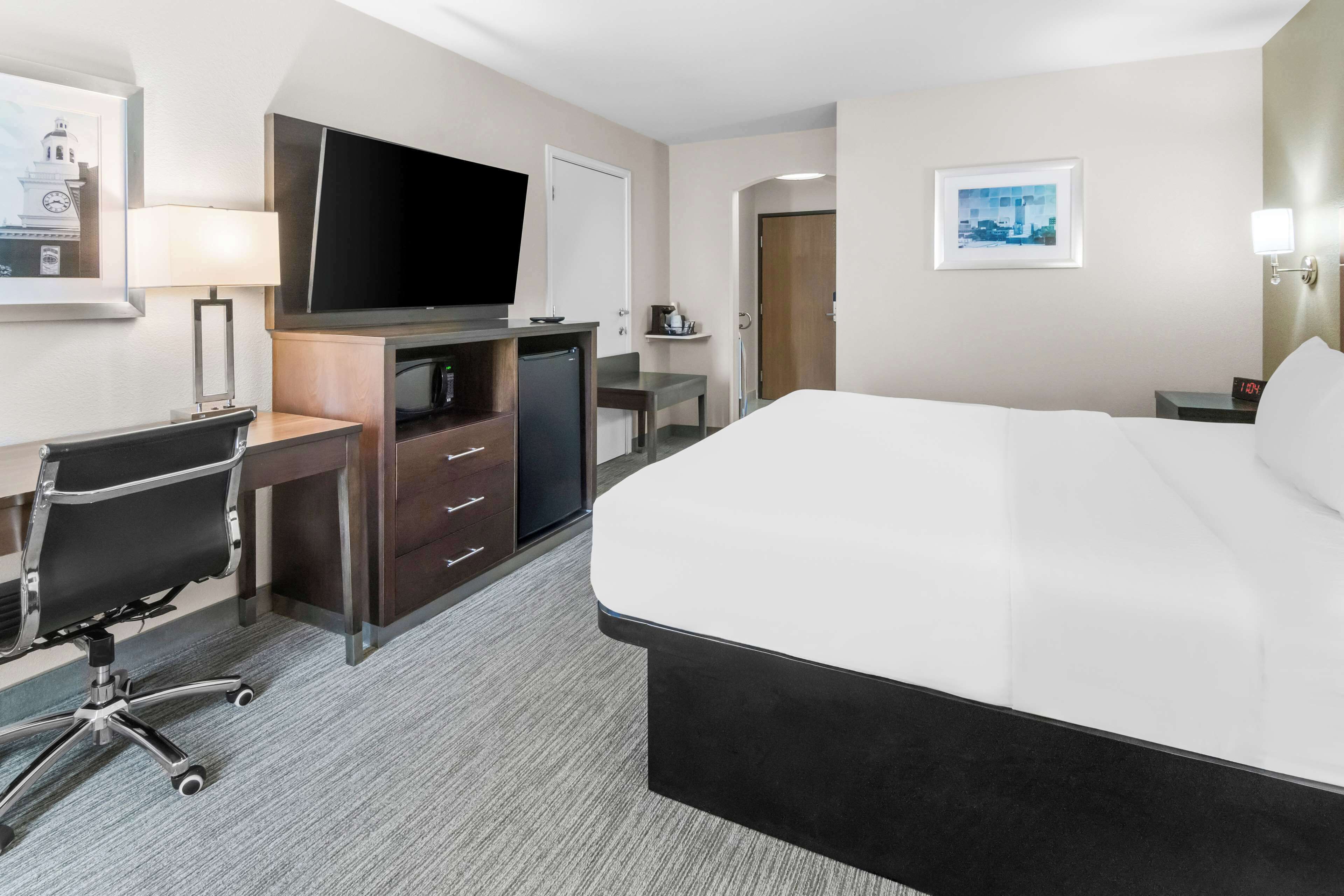 Une chambre d’hôtel avec un grand lit, un bureau avec une chaise, une télévision et un petit réfrigérateur.