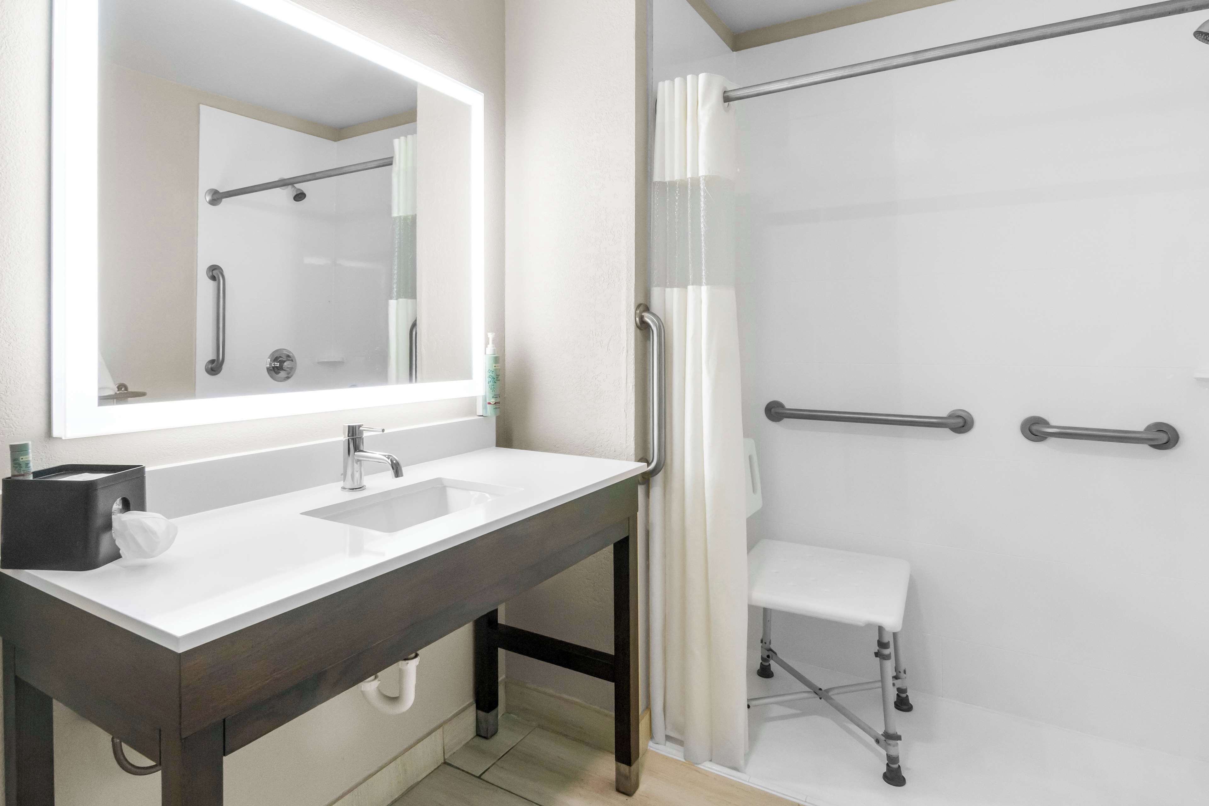 Un baño moderno con un lavabo blanco, tocador de madera oscura, un espejo grande y una cabina de ducha con mampara de vidrio.