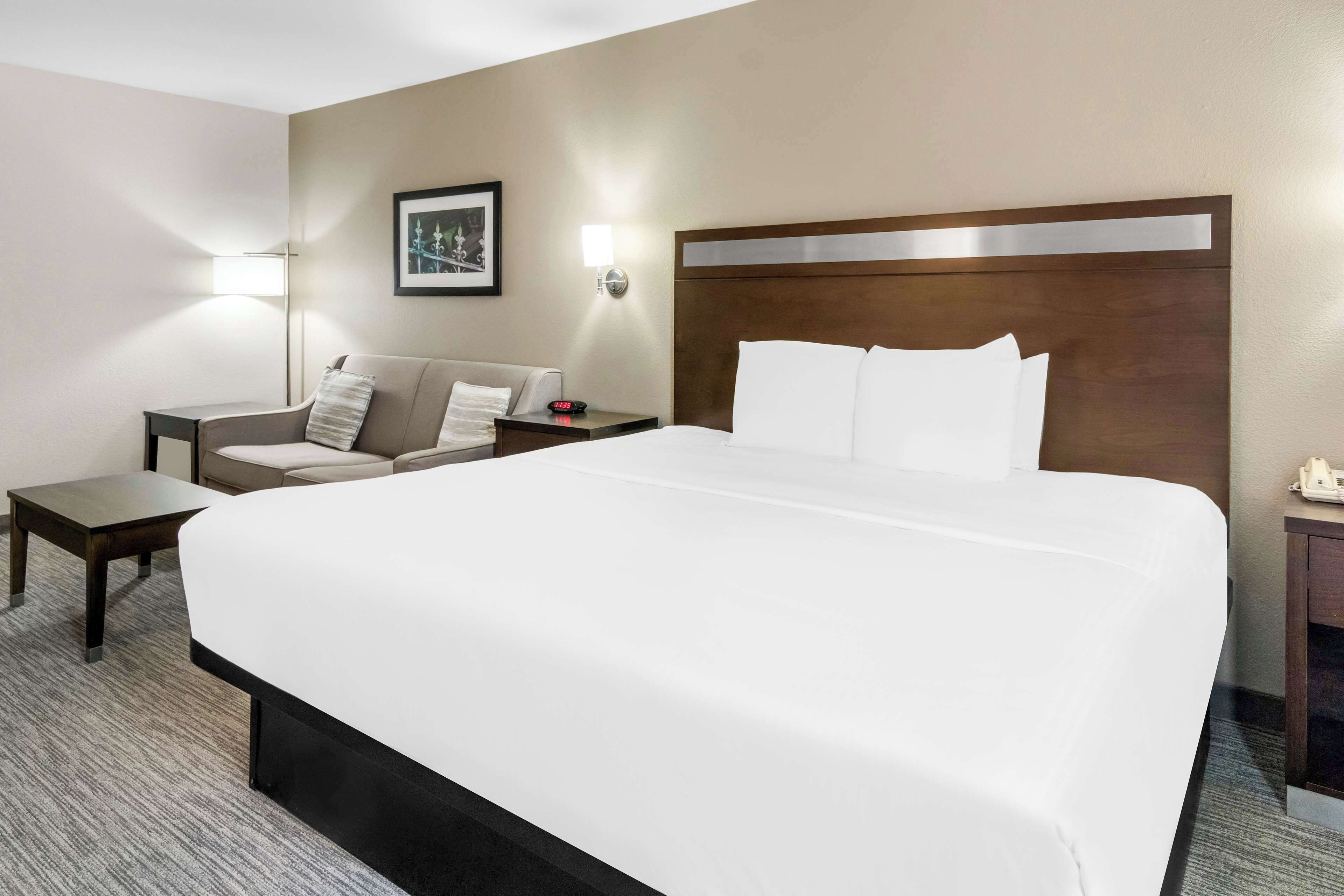 Una habitación de hotel con una cama grande, un sofá, una mesita y una mesita de noche con lámpara.