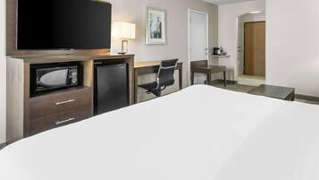 A hotel room with a bed, a desk with a chair, a television, a microwave, a coffee machine, and a framed picture on the wall.