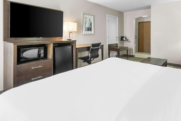 A hotel room with a bed, a desk with a chair, a television, a microwave, a coffee machine, and a framed picture on the wall.