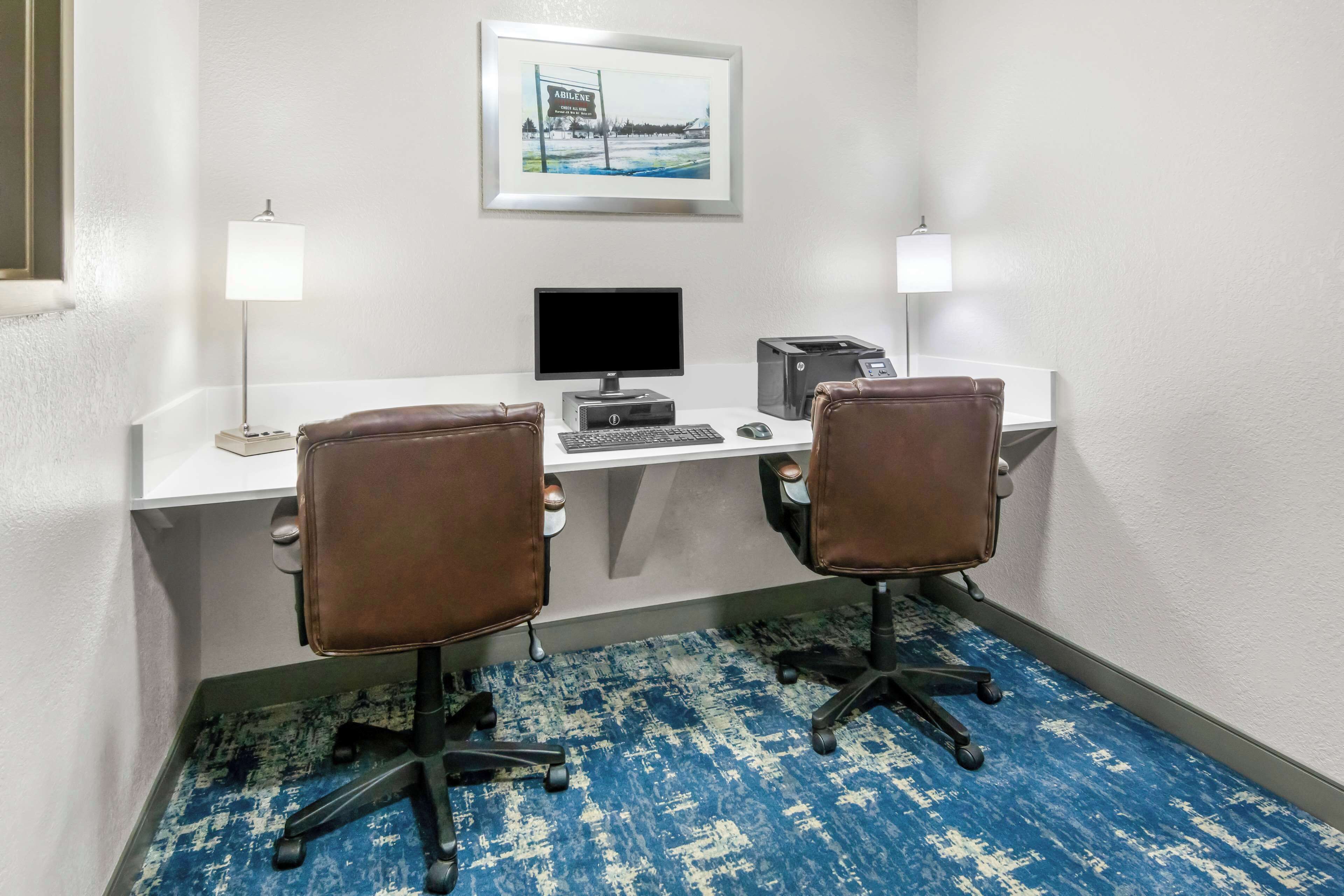 Habitación de hotel con un escritorio, dos sillas, una computadora y un cuadro en la pared.