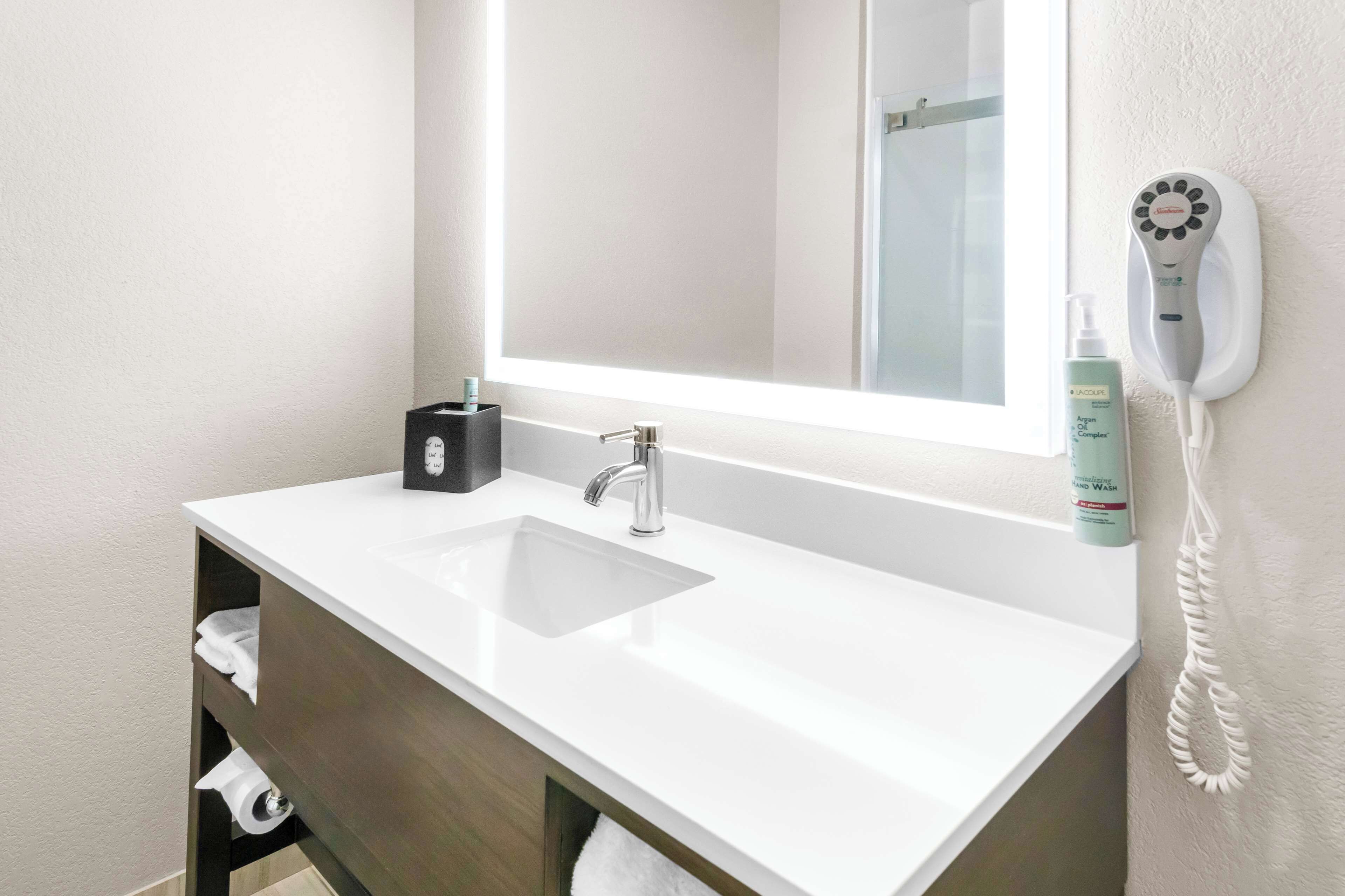 Une salle de bain moderne avec un lavabo blanc, un miroir et un sèche-cheveux fixé au mur.
