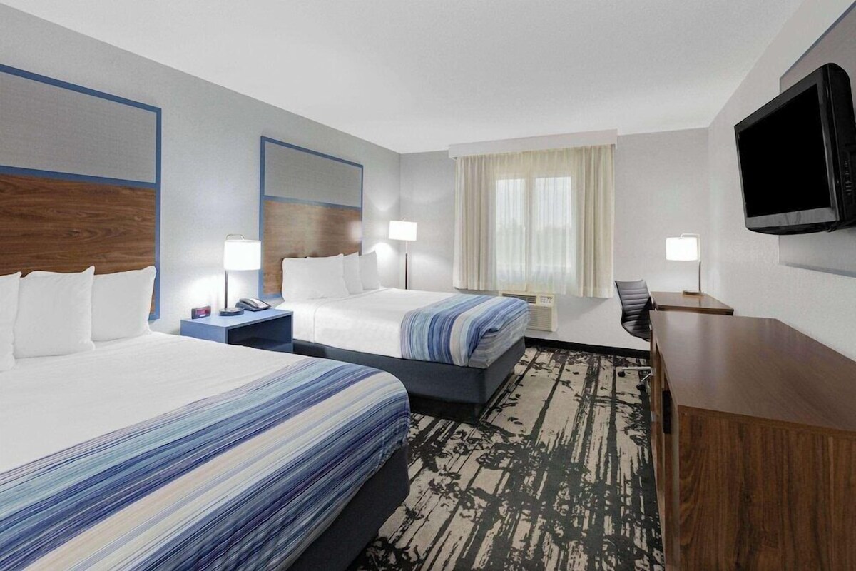 A hotel room with two beds, a desk, a TV, and a window with curtains.