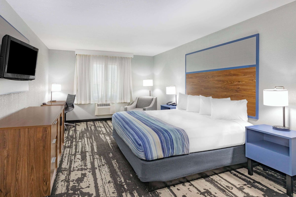 A hotel room with a large bed, a desk, a chair, a TV, and a window with curtains.