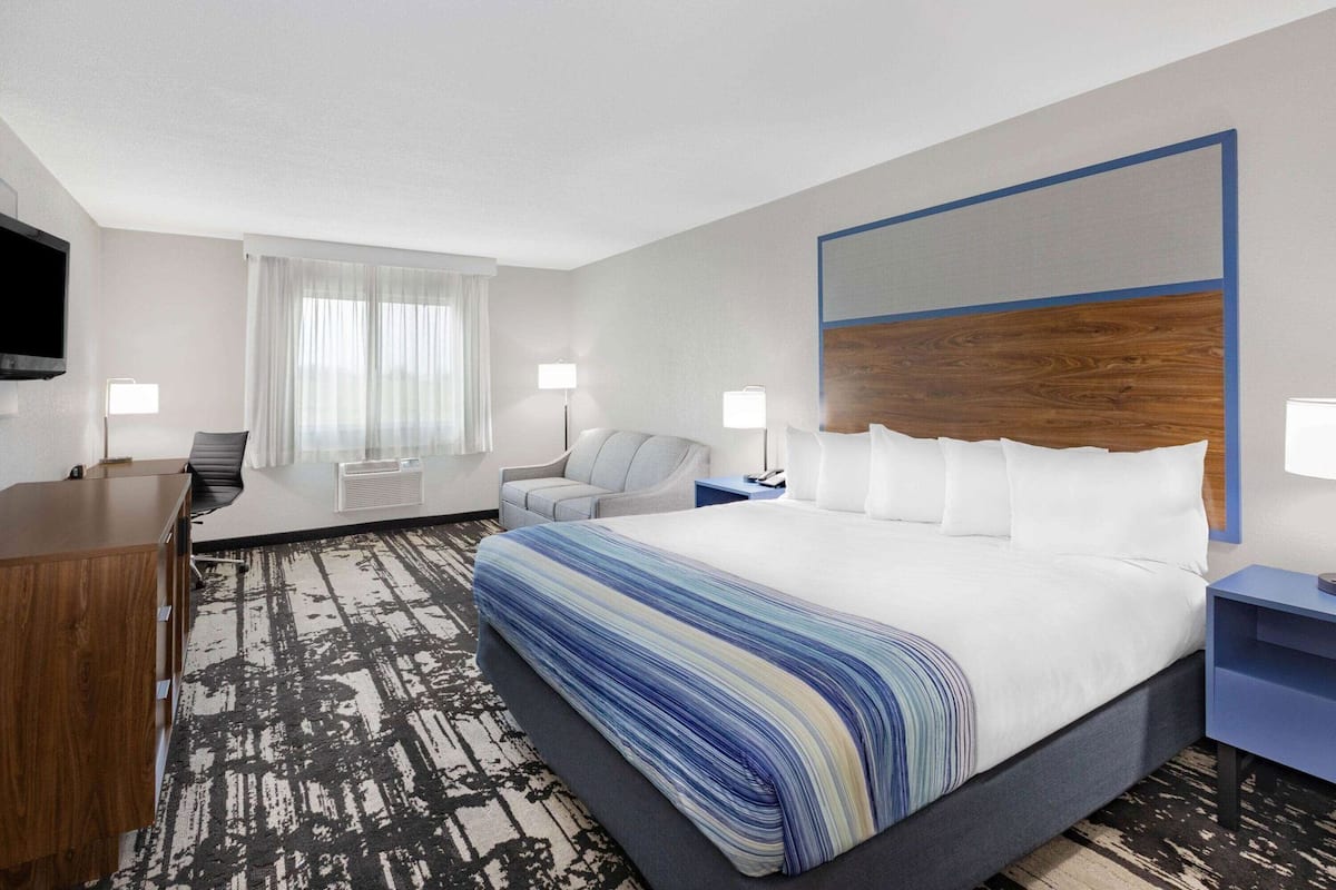 A hotel room with a large bed, a desk, a chair, a TV, and a window with curtains.