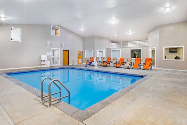 A swimming pool with a metal ladder, orange lounge chairs, and a ceiling with recessed lighting. - AmericInn by Wyndham Pella (Pella)