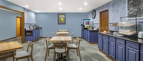 Un restaurante con paredes azules, mesas y sillas de madera. Hay armarios azules y un menú en una pizarra en la pared.