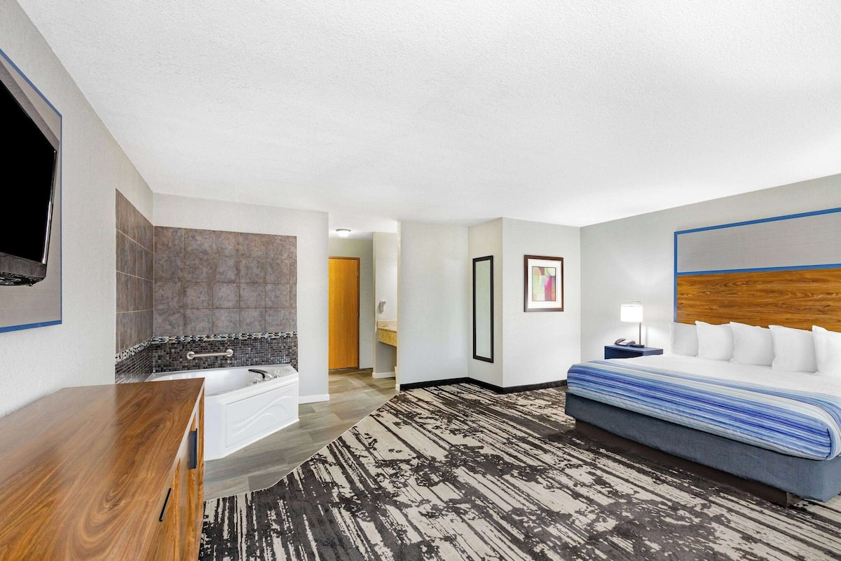 A hotel room with a large bed, a wooden dresser, a bathtub, and a television mounted on the wall.