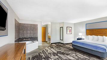 A hotel room with a large bed, a wooden dresser, a bathtub, and a television mounted on the wall.