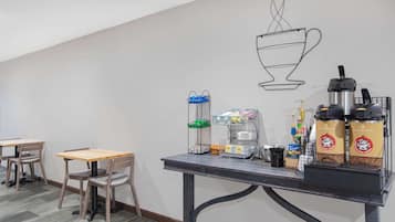 A coffee station with a coffee machine, cups, and a coffee bag. There are two tables and chairs.