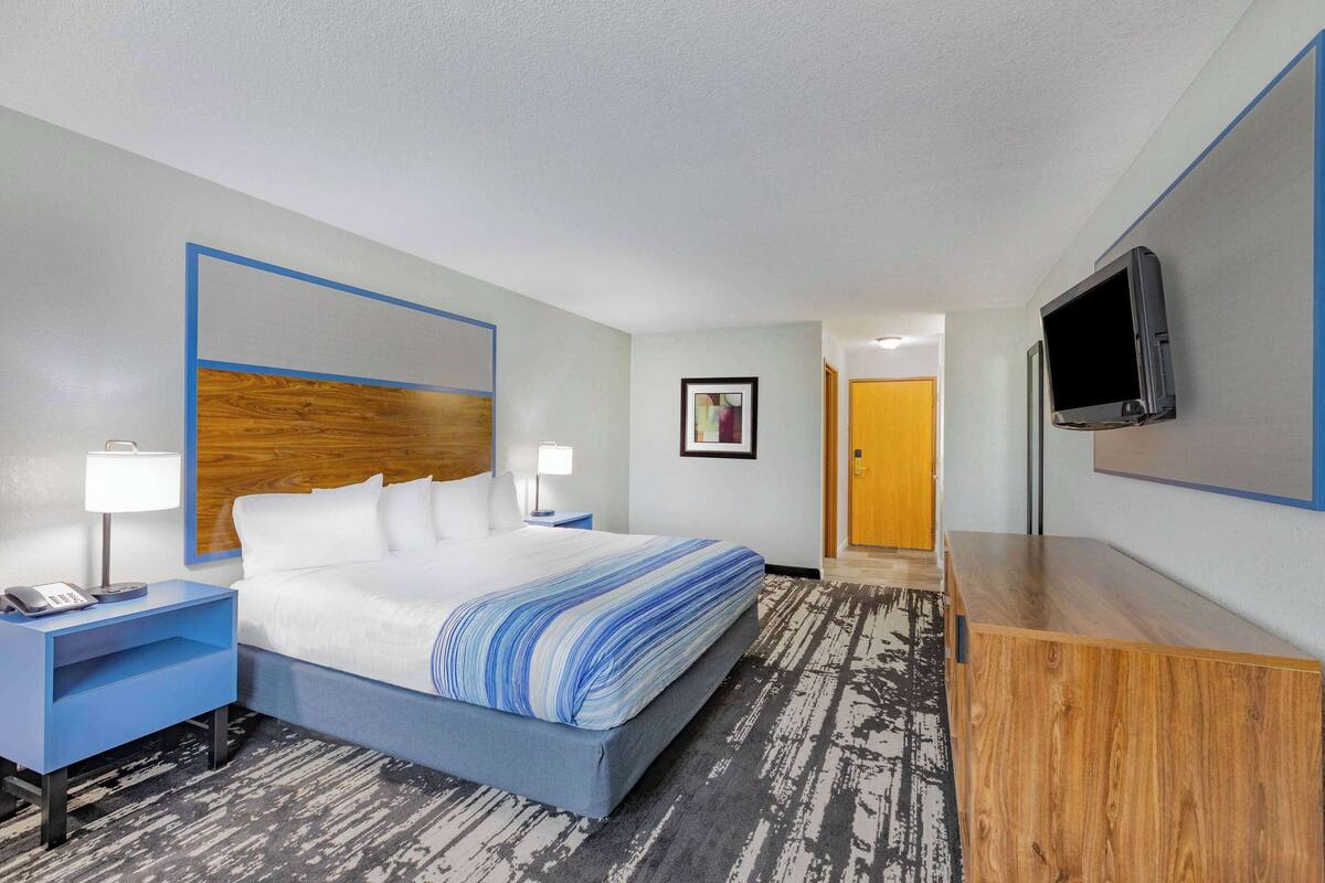 A hotel room with a bed, bedside tables, a TV, and a wooden dresser.