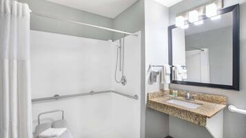 A modern bathroom with a shower, grab bar, sink, and mirror.