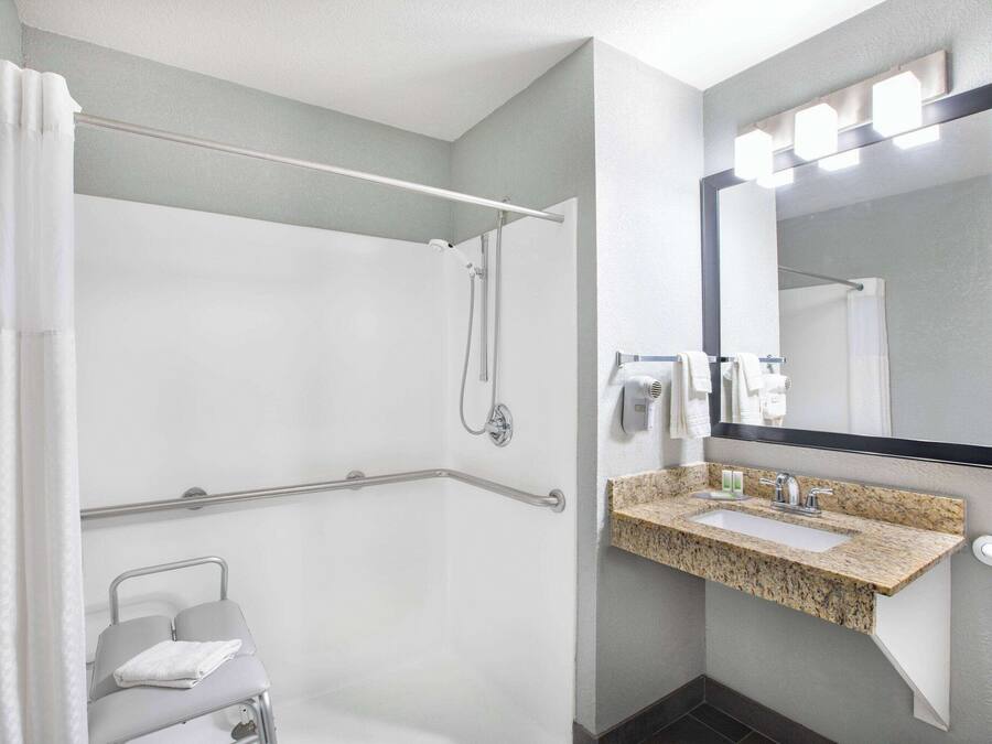 A modern bathroom with a shower, grab bar, sink, and mirror.