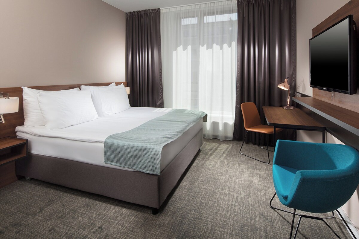 Een hotelkamer met een bed, een bureau, een stoel, een televisie en een lamp.