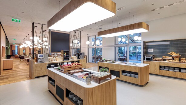 A modern cafe with wooden counters, a coffee machine, and a variety of food items displayed. - Holiday Inn Prague Congress Centre by IHG (Prague)