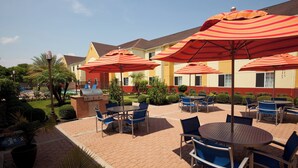 Une terrasse extérieure avec des tables et des chaises, entourée de parasols à rayures, et une piscine en arrière-plan.