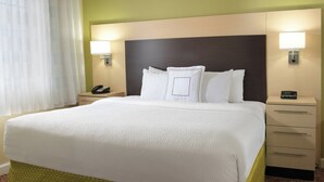 Une chambre d’hôtel avec un grand lit, deux tables de chevet, une petite table avec un téléphone et deux lampes fixées au mur.