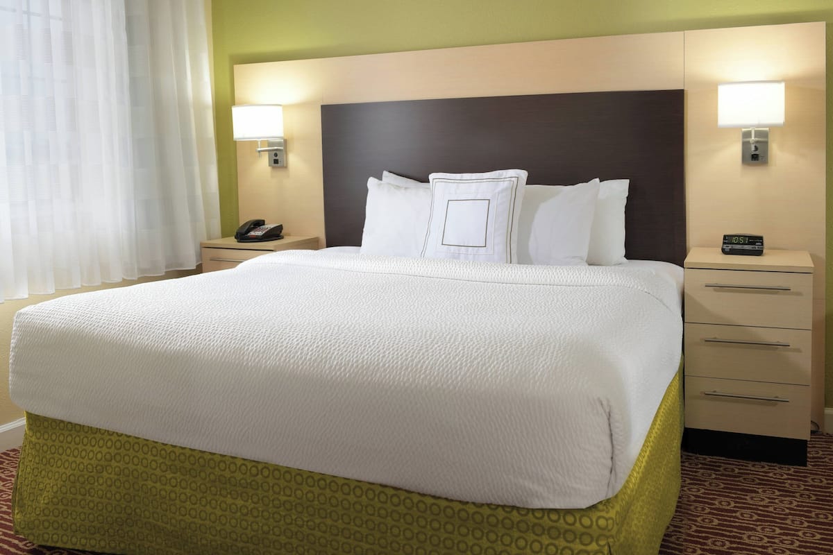 Hotelkamer met een groot bed, twee nachtkastjes, een bijzettafeltje met een telefoon, en twee wandlampen.