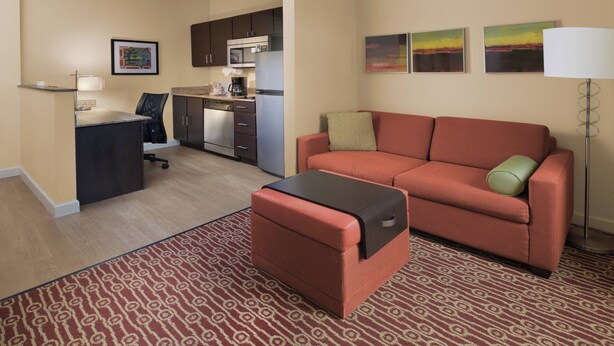Un espace de vie compact comprenant un coin cuisine, un canapé, une petite table et un tapis à motifs.