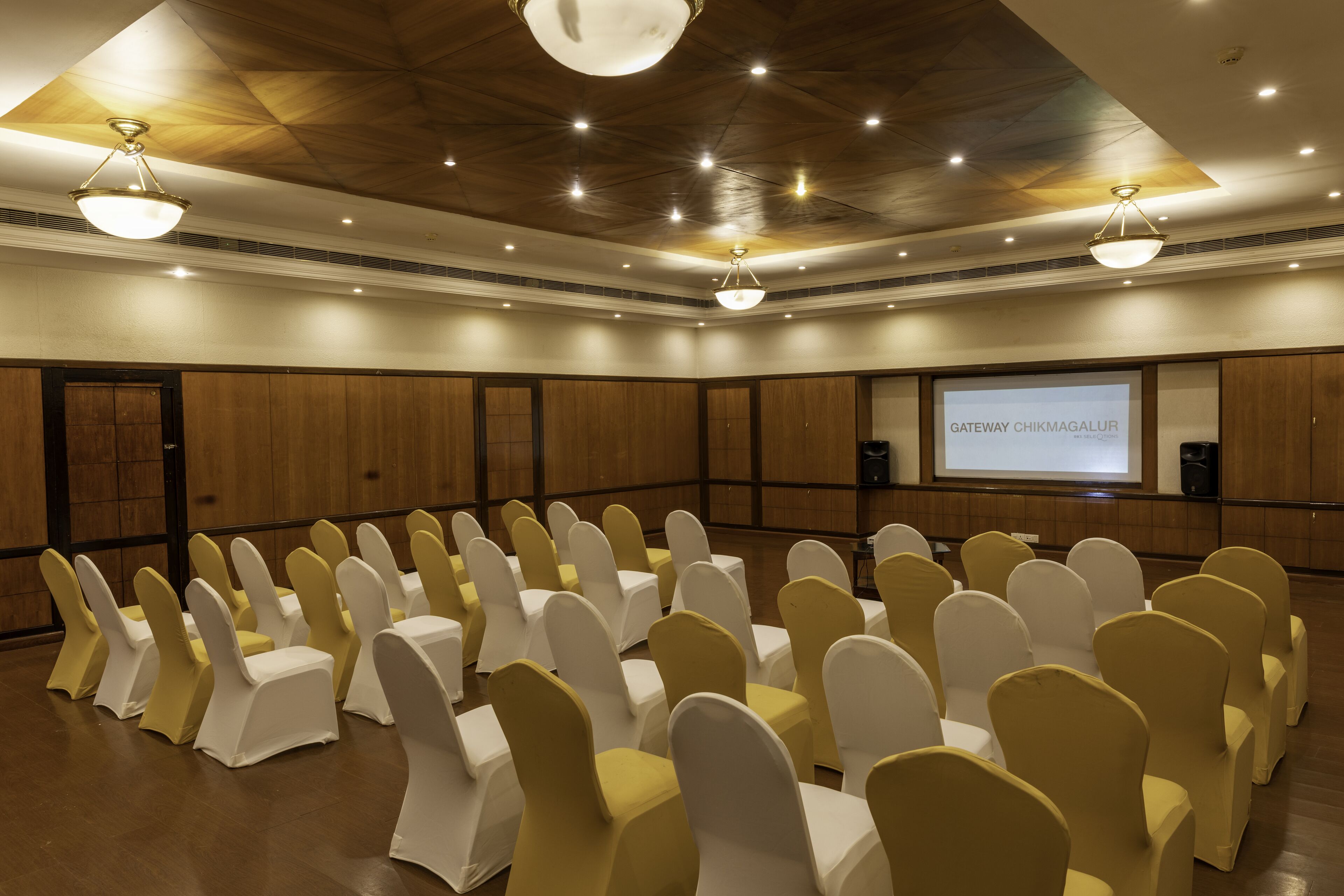 A conference room with rows of chairs, a projector screen, and a wooden ceiling.