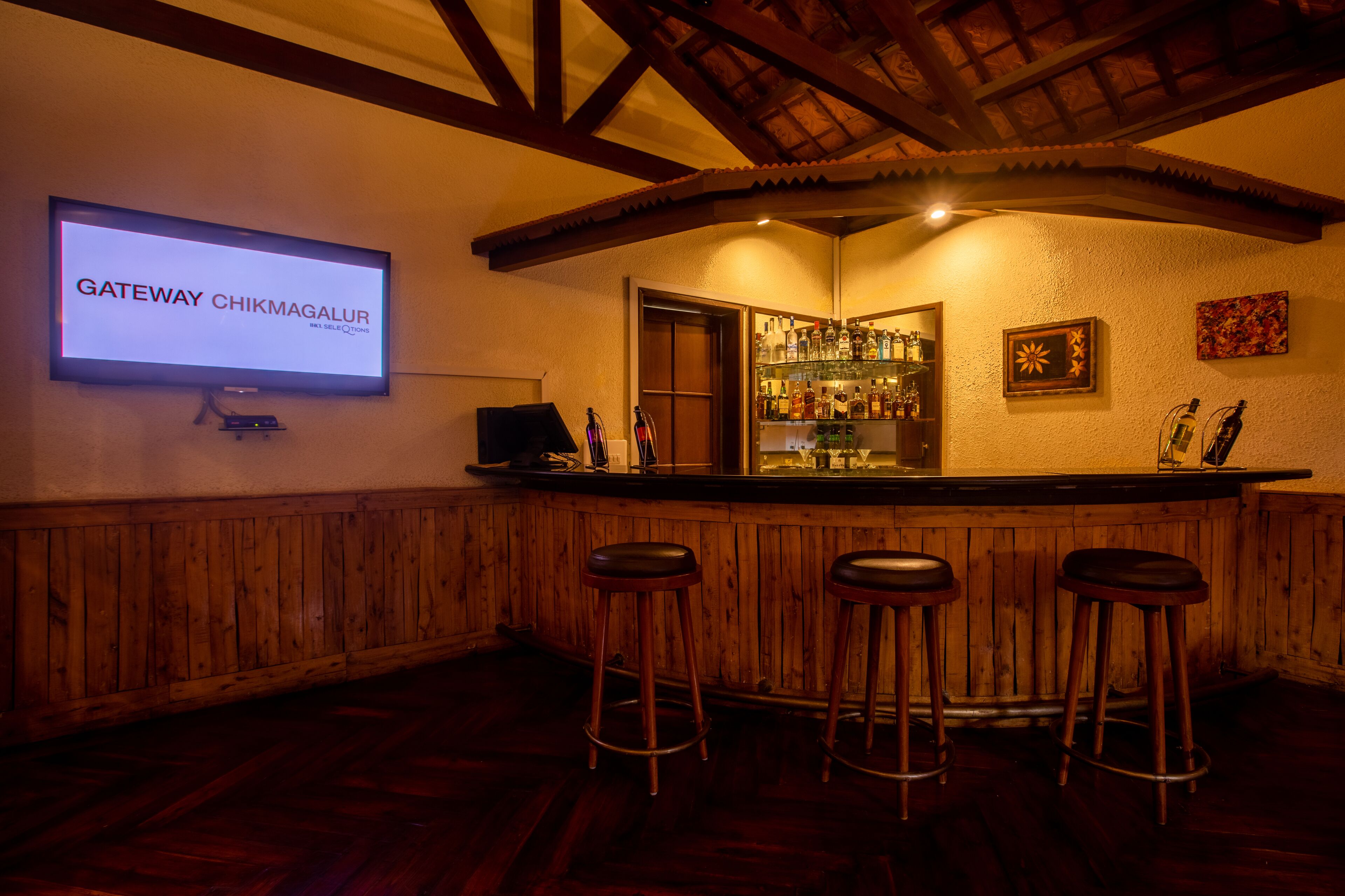 Una zona de bar con taburetes de madera, una pantalla de televisión mostrando 