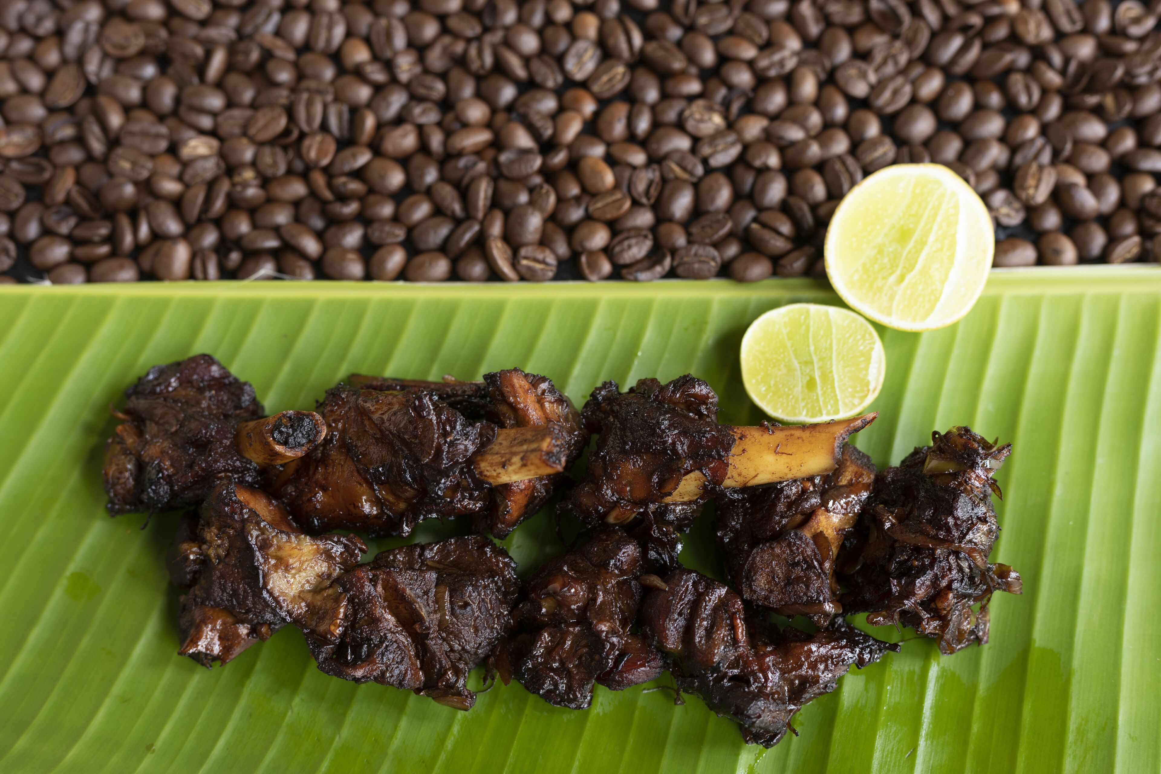 Carne a la parrilla en un plato verde con dos gajos de lima, rodeada de granos de café.