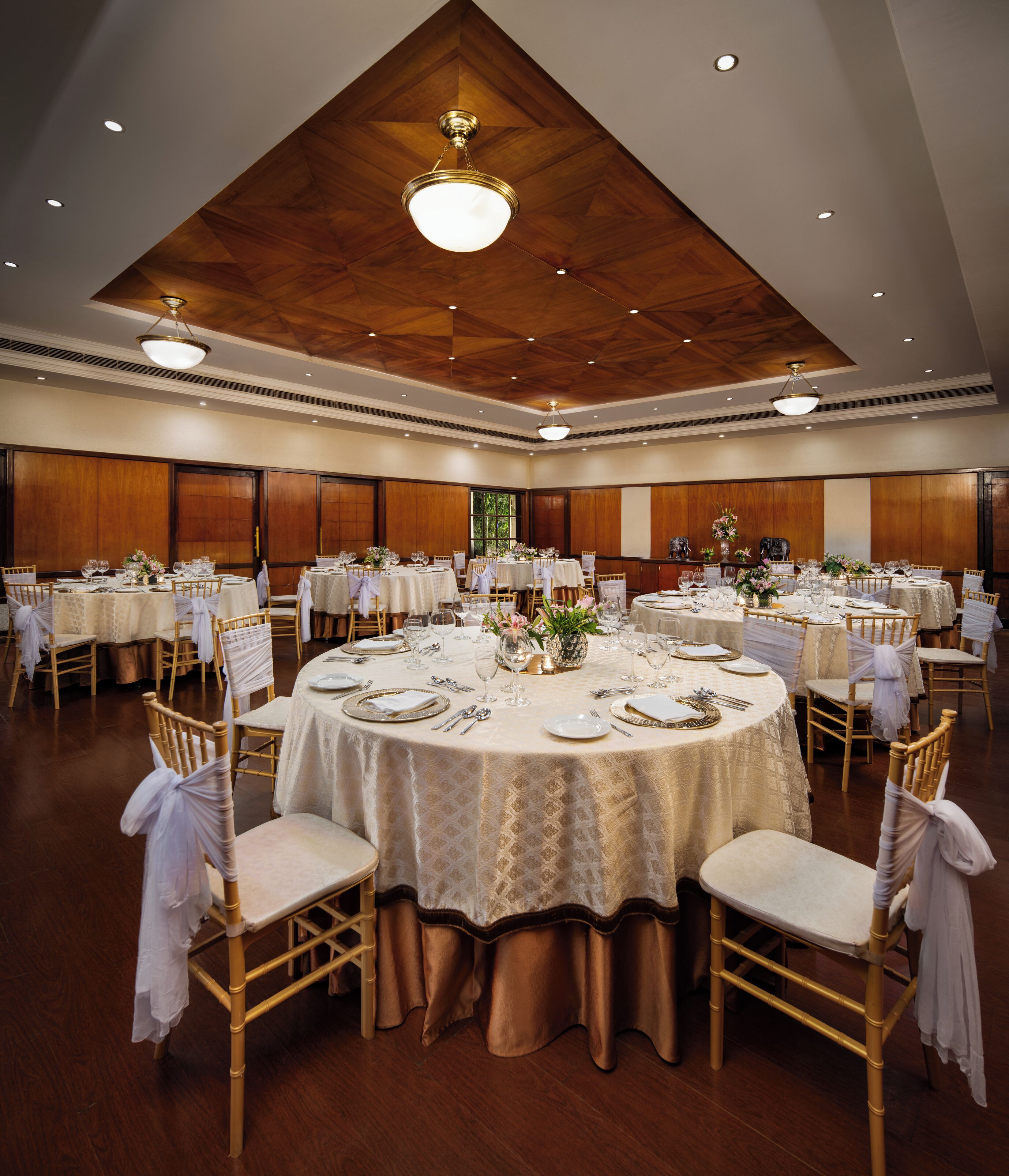 Un salón de banquetes con mesas redondas, manteles blancos y sillas doradas.