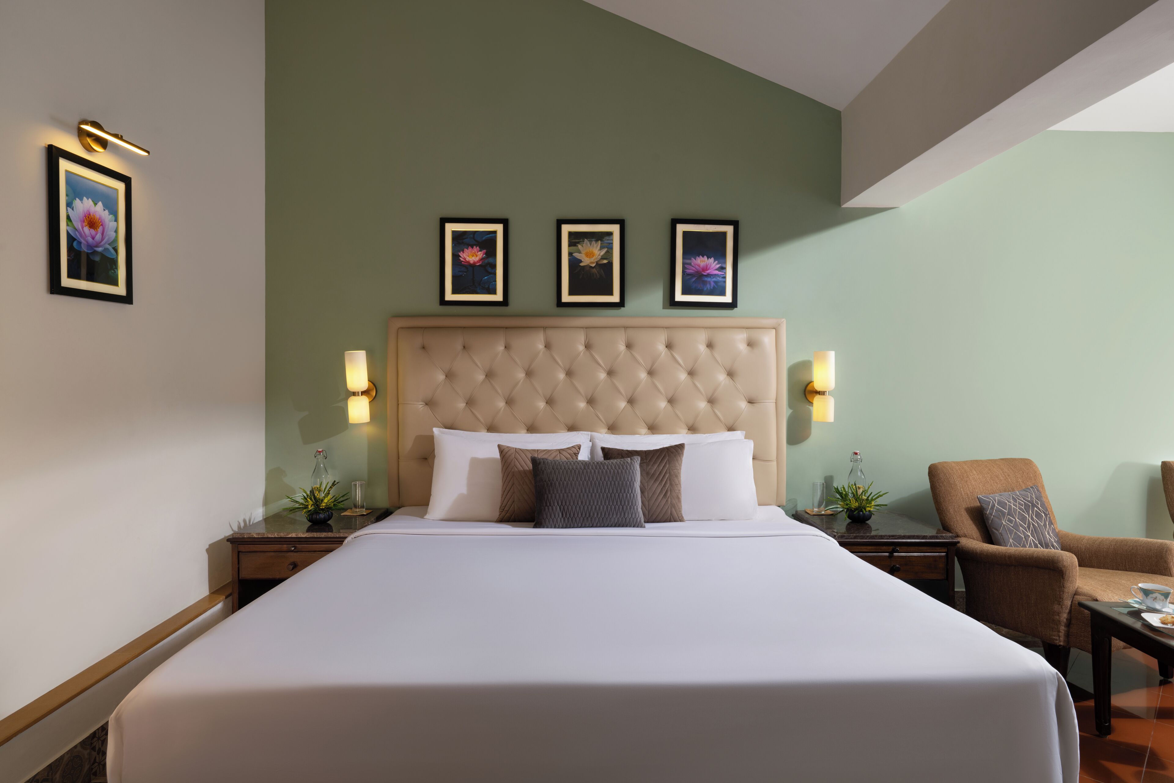 Habitació d'hotel amb un llit gran, un panell de capçal tapissat, tres quadres florals enmarcades a la paret, dues taules de nit amb làmpades i un armari marró.
