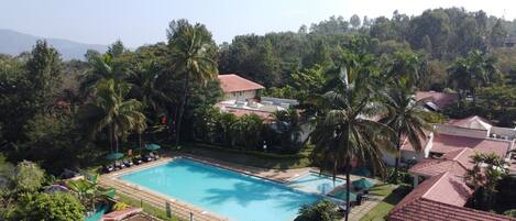 A swimming pool surrounded by palm trees and a building with a red-tiled roof.