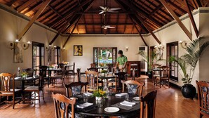 A spacious dining area with wooden tables and chairs, a high ceiling with exposed beams, and a ceiling fan. - Gateway Chikmagalur (Chikkamagaluru)