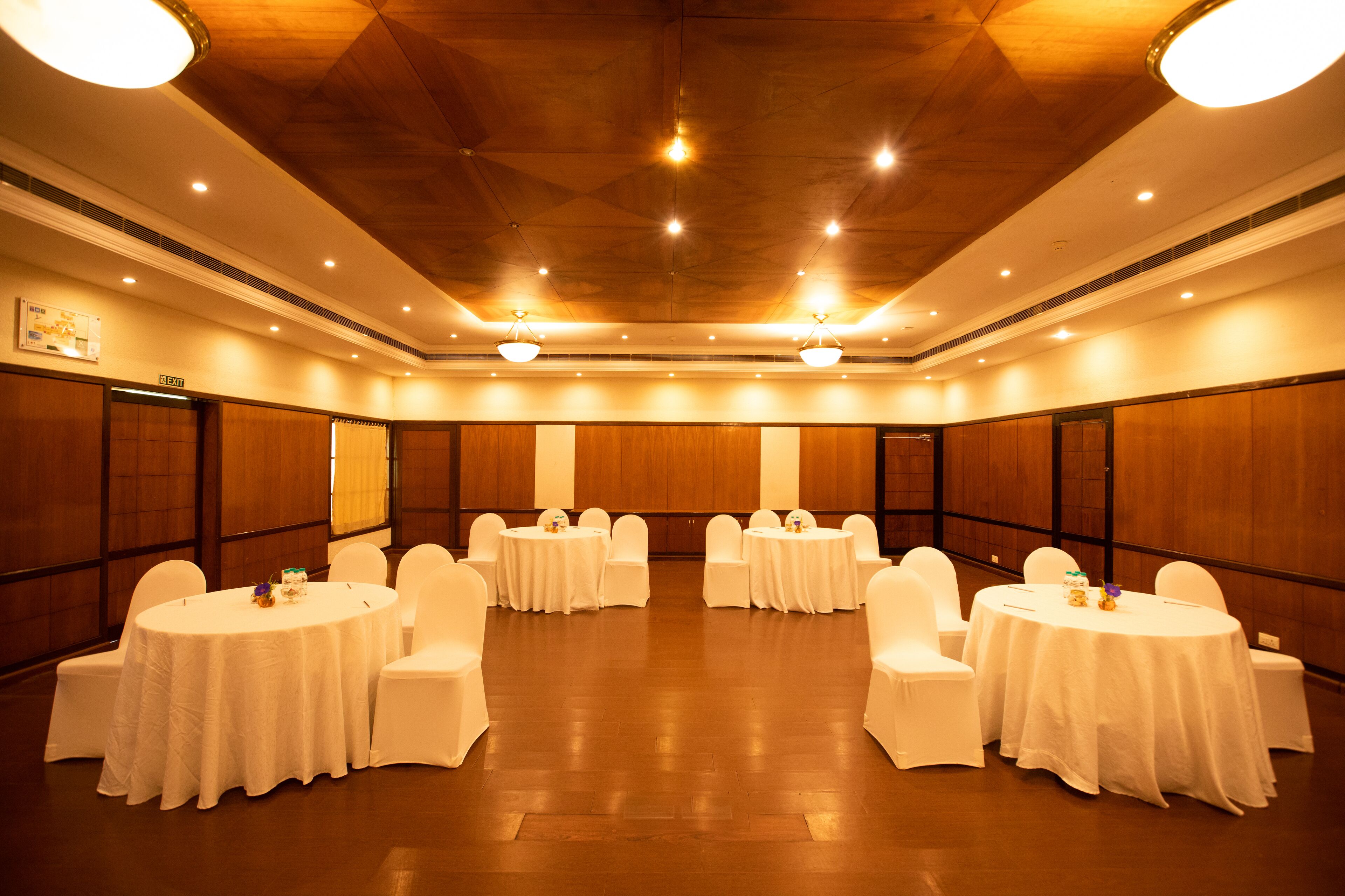 Un salón de conferencias con mesas redondas, sillas blancas y paneles de madera.