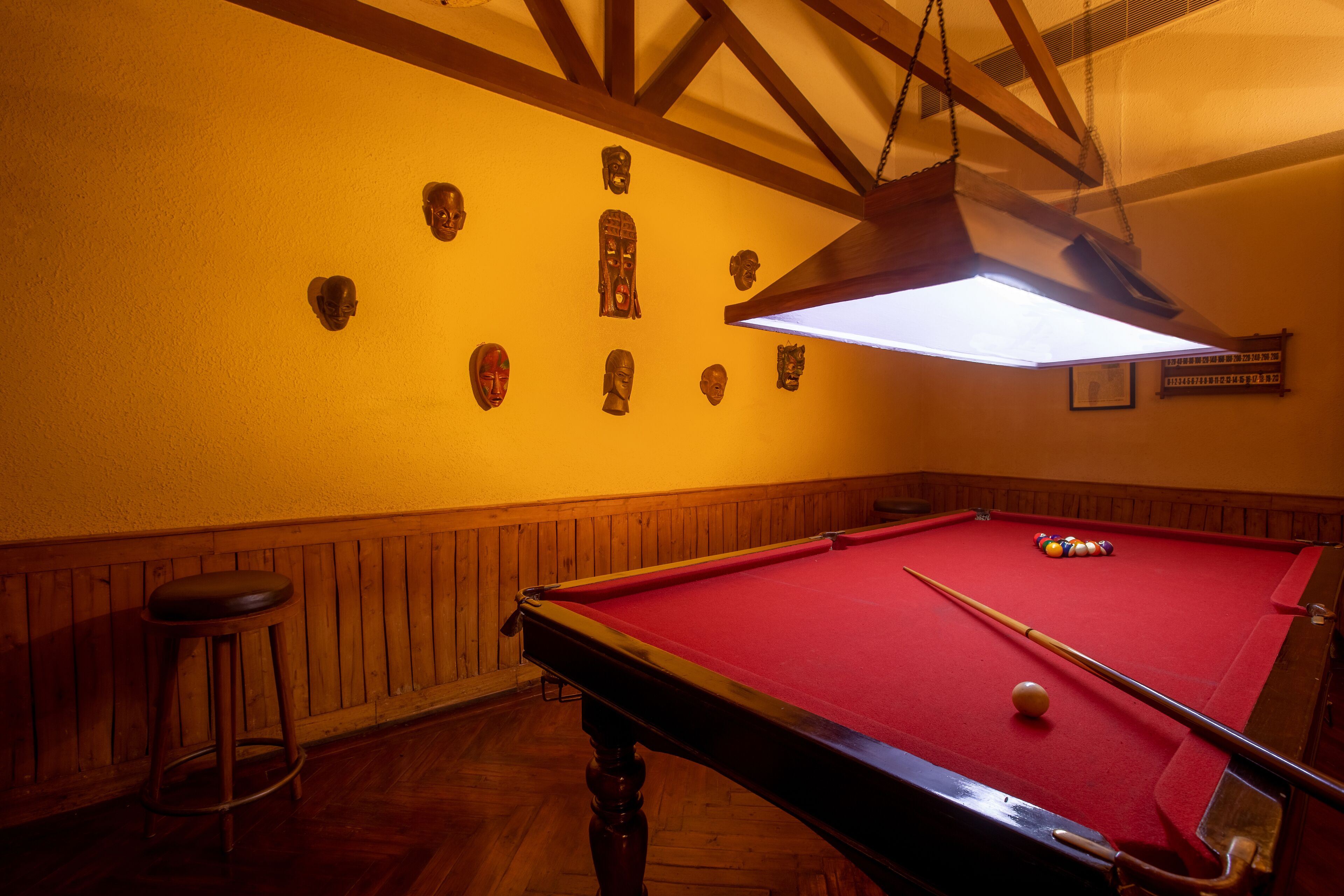 A pool table with a red felt surface, surrounded by wooden paneling and a wooden stool.