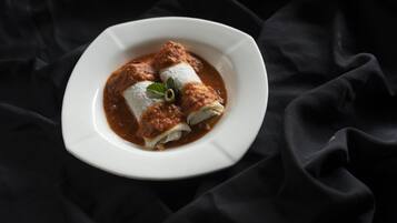 Un plato de enchiladas con salsa oscura, adornado con una hoja verde, sobre un plato blanco frente a un fondo de tela oscura.