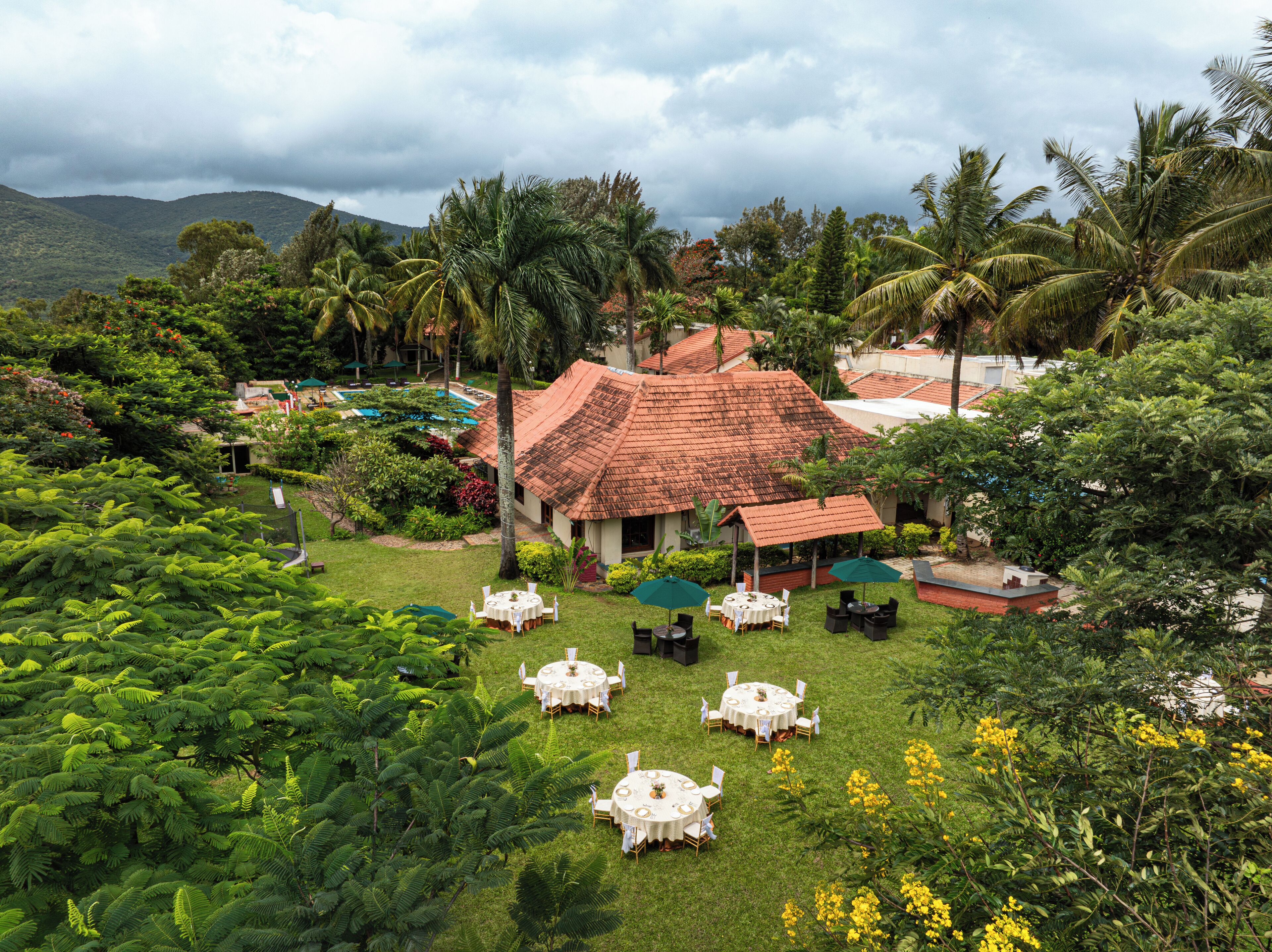 A tropical resort with a thatched-roof building, outdoor dining area, and lush greenery.