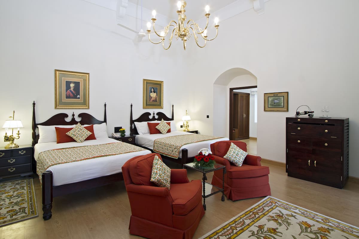 Une chambre d’hôtel avec deux lits, un lustre, une commode et un fauteuil rouge.