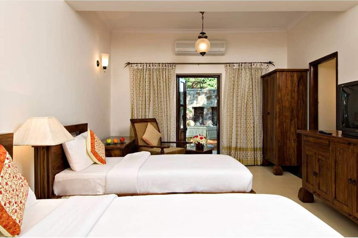 Une chambre d’hôtel avec deux lits, une télévision, une armoire en bois, une chaise et une table avec une lampe et des fleurs.