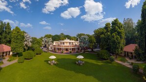 A large, two-story house with a circular driveway, surrounded by well-maintained lawns and trees. - The Maharaja's Lodge, Ranthambore (Sawai Madhopur)