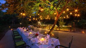 An outdoor dining area with tables set for a meal, surrounded by trees and string lights. - The Maharaja's Lodge, Ranthambore (Sawai Madhopur)