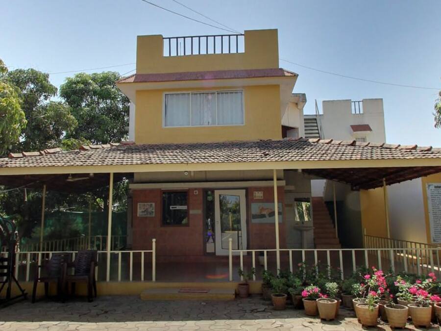 A two-story building with a covered porch, potted plants, and a staircase leading to the entrance.