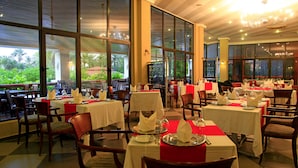 A restaurant with tables set for dining, large windows, and a view of greenery outside. - The Kairaba Beach Hotel (Serrekunda)