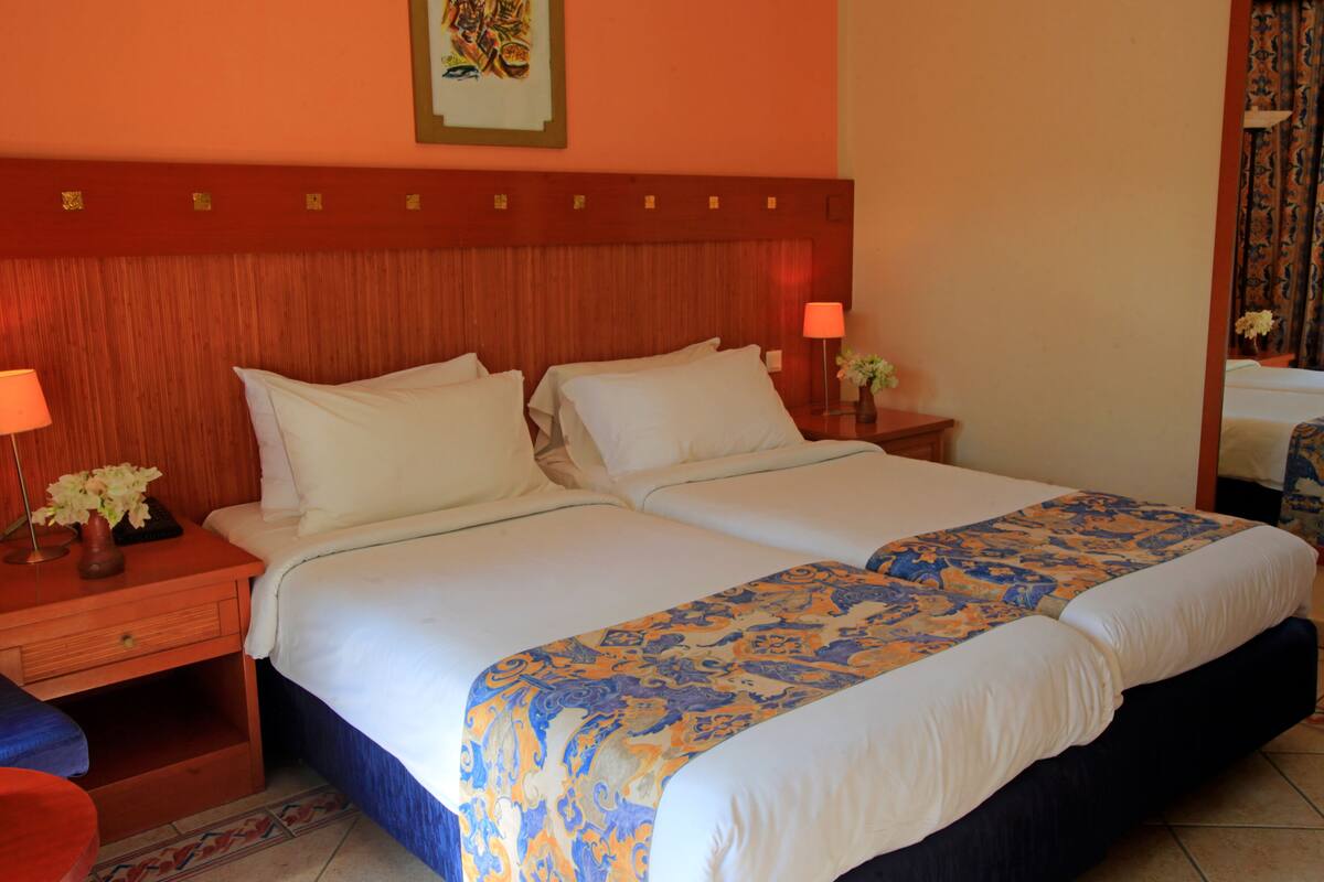 A double bed with a patterned bedspread, a nightstand with a lamp, and a vase of flowers.