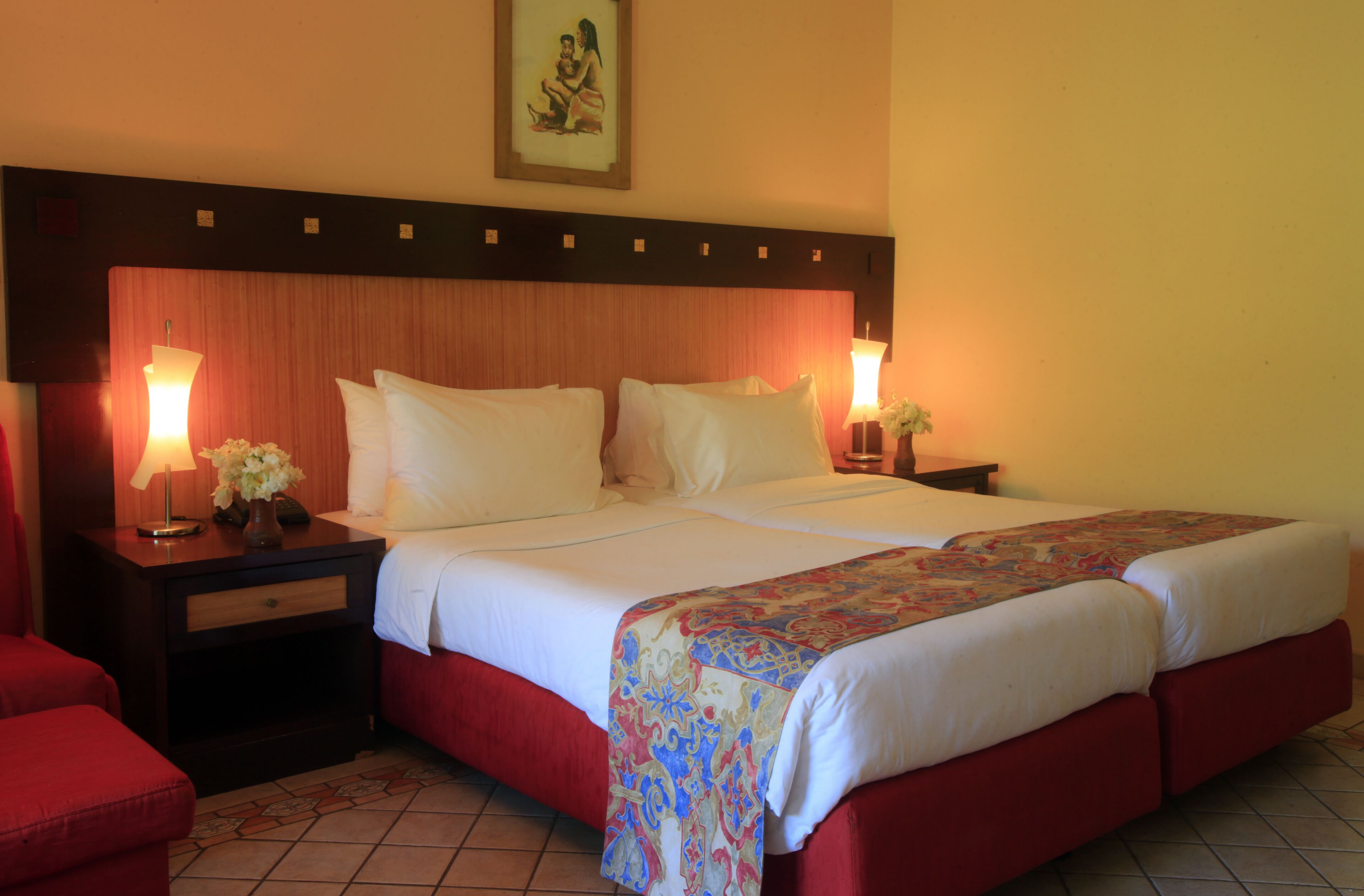 Une chambre d’hôtel avec un grand lit, deux tables de chevet avec des lampes, un fauteuil rouge et un élément décoratif mural.