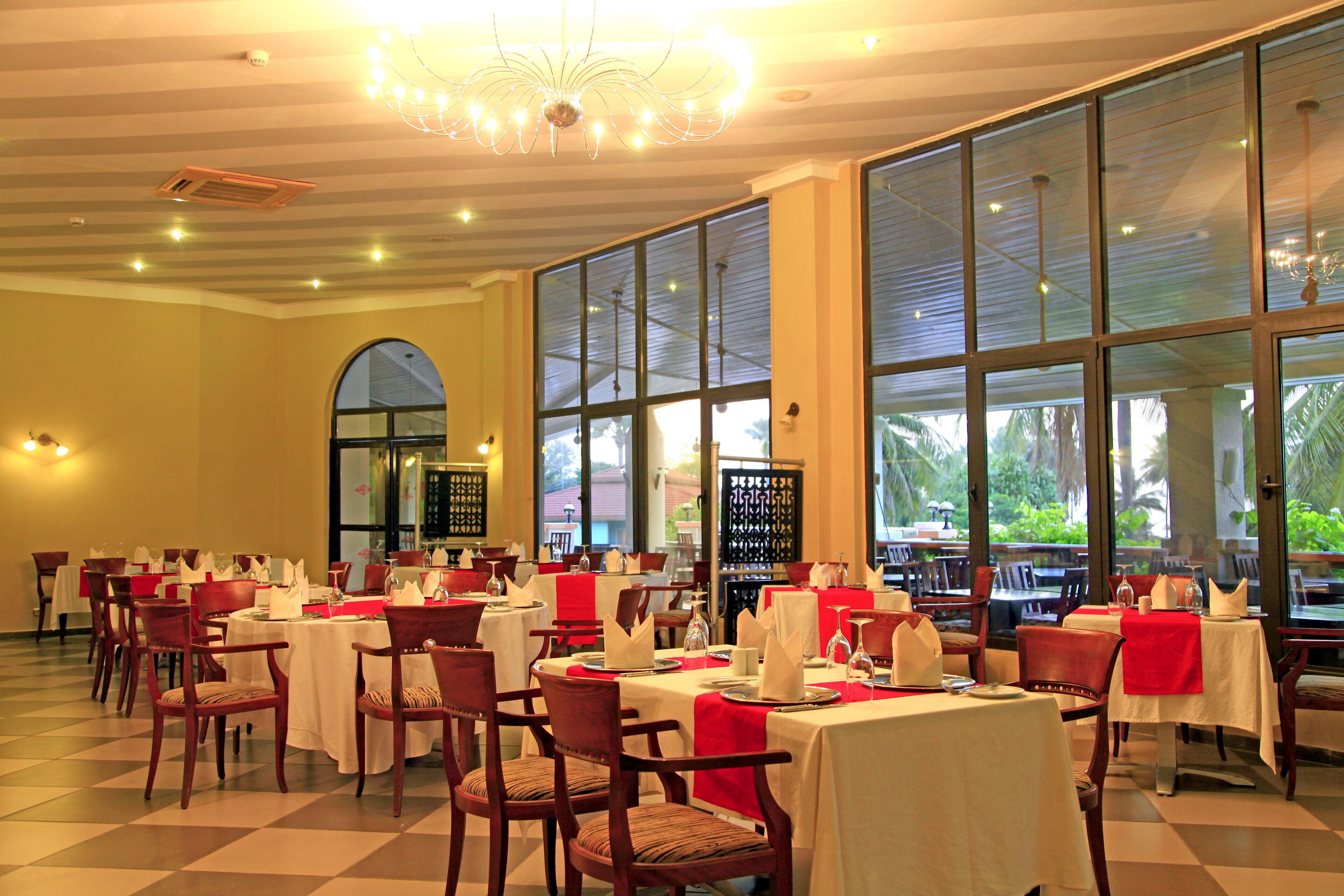 Un restaurante con varias mesas y sillas, ventanas amplias y un candelabro.