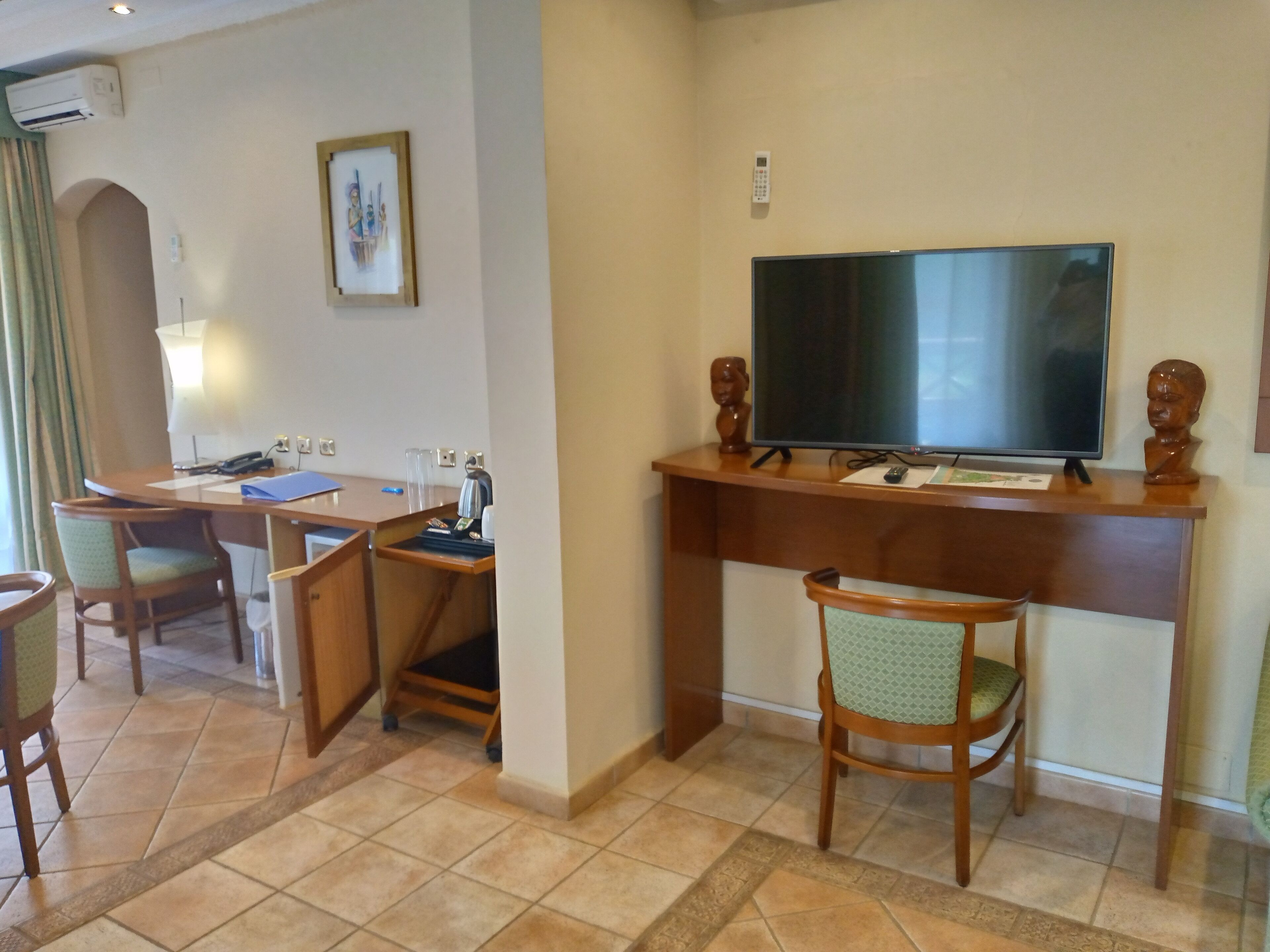 Habitación de hotel con escritorio, sillas, televisor y una pequeña estatua.