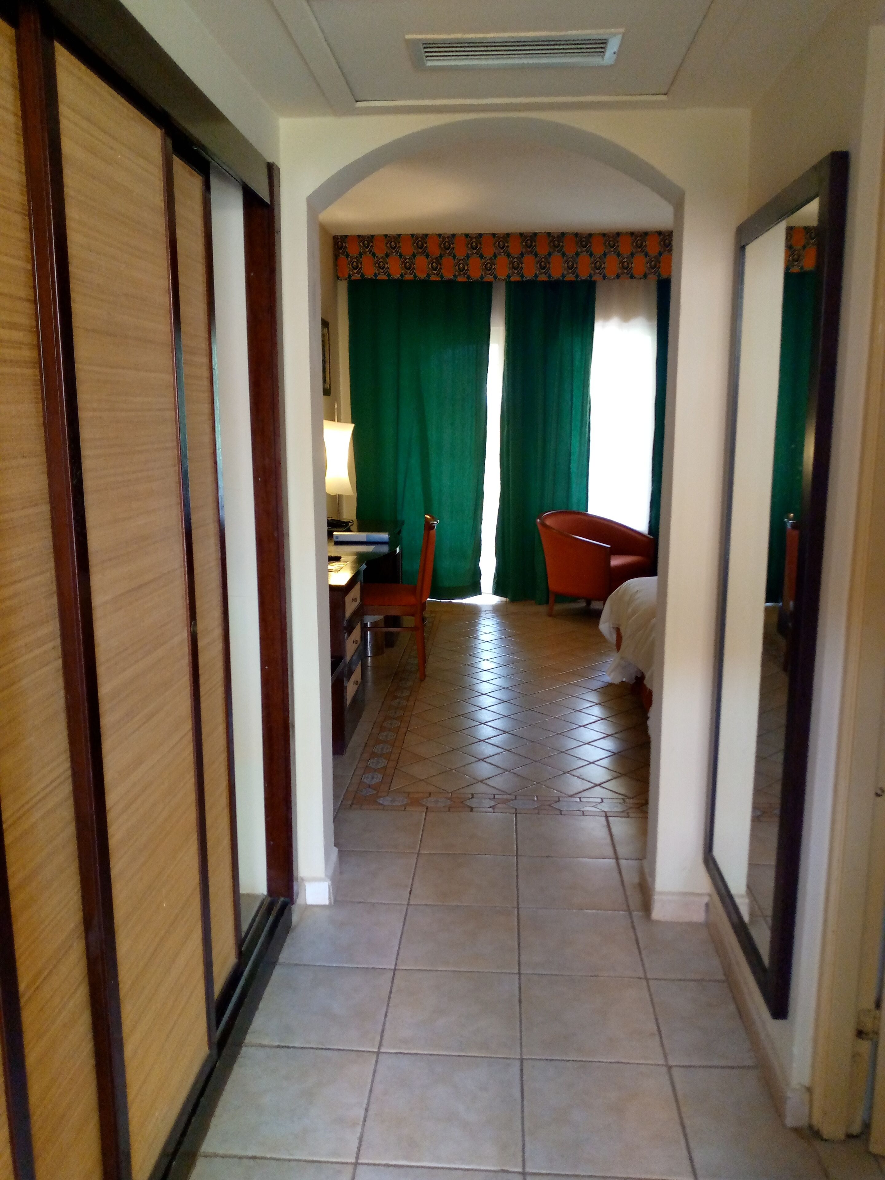 Un pasillo de hotel con una puerta de madera, un escritorio con lámpara, una silla y una cama.
